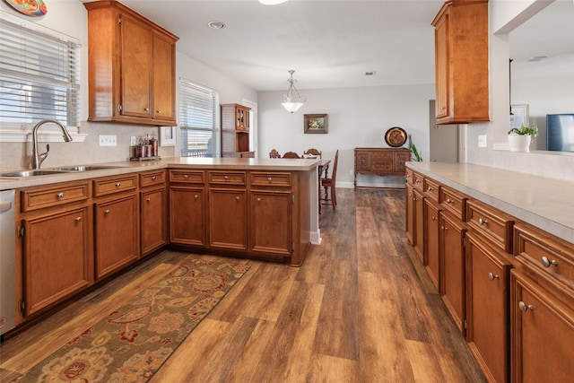 kitchen featuring a peninsula, light countertops, a sink, brown cabinets, and dark wood-style floors