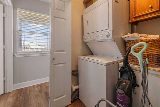 laundry area featuring laundry area, baseboards, stacked washer / dryer, and wood finished floors