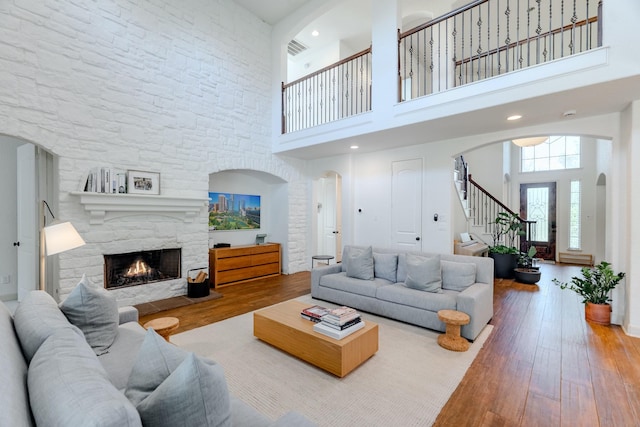living room featuring a high ceiling, a fireplace, arched walkways, hardwood / wood-style floors, and stairs