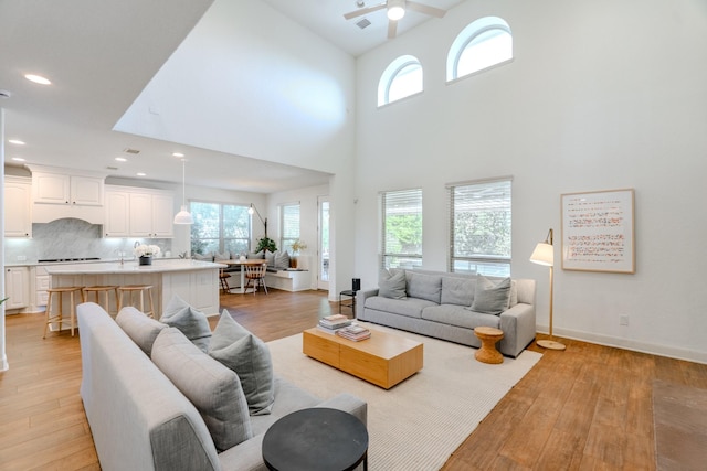 living room featuring baseboards, ceiling fan, a high ceiling, light wood-type flooring, and recessed lighting