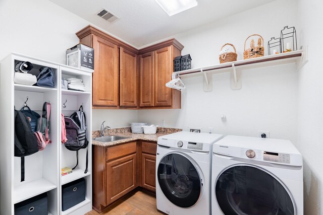 clothes washing area with visible vents, cabinet space, a sink, light wood-style floors, and separate washer and dryer