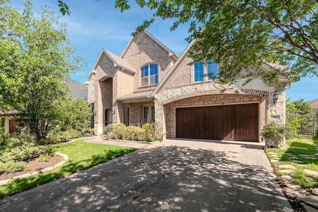 french country style house featuring an attached garage, driveway, stone siding, and brick siding