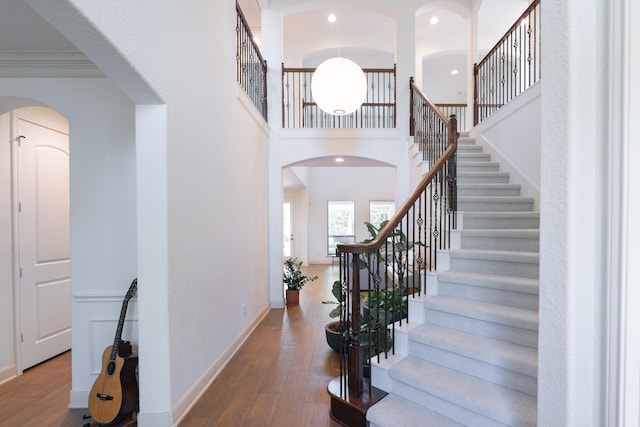 entryway featuring a towering ceiling, arched walkways, wood finished floors, stairway, and baseboards