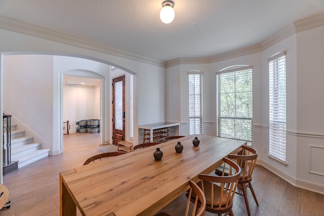dining space featuring arched walkways, stairway, baseboards, light wood-style floors, and ornamental molding