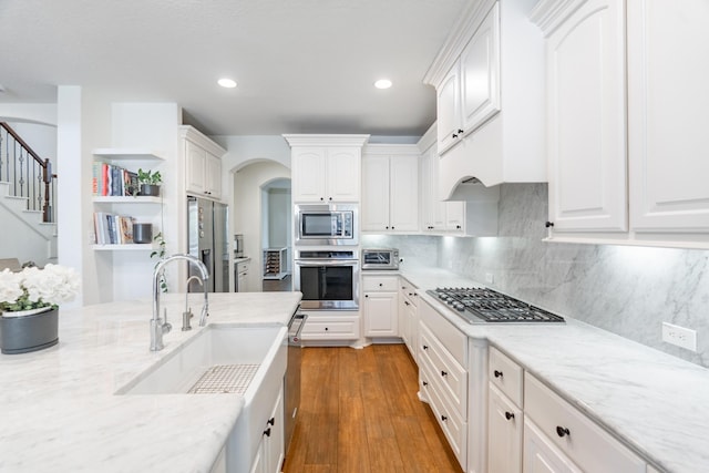 kitchen with appliances with stainless steel finishes, arched walkways, open shelves, a sink, and white cabinetry