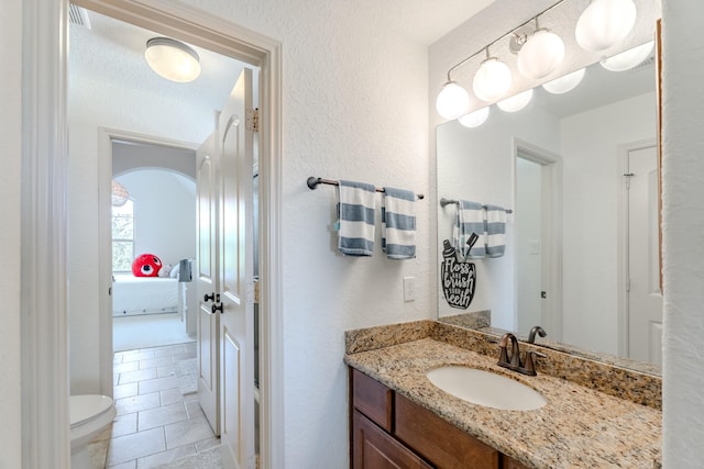bathroom featuring vanity, tile patterned flooring, a textured wall, toilet, and connected bathroom