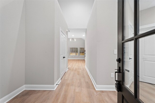 corridor featuring baseboards, vaulted ceiling, and light wood-style floors