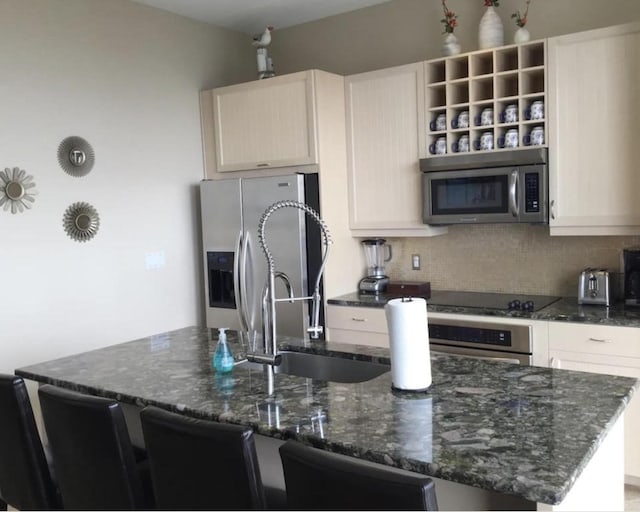 kitchen with an island with sink, tasteful backsplash, a breakfast bar, dark stone countertops, and stainless steel appliances