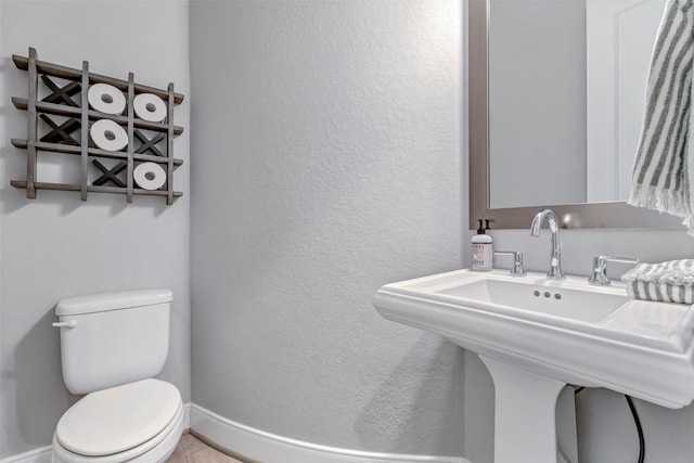 half bathroom featuring toilet, a textured wall, and a sink