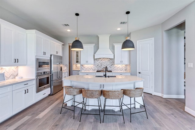 kitchen featuring visible vents, a sink, appliances with stainless steel finishes, custom range hood, and backsplash