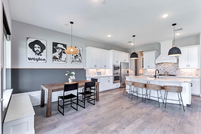 kitchen with visible vents, light countertops, a kitchen bar, custom range hood, and decorative backsplash
