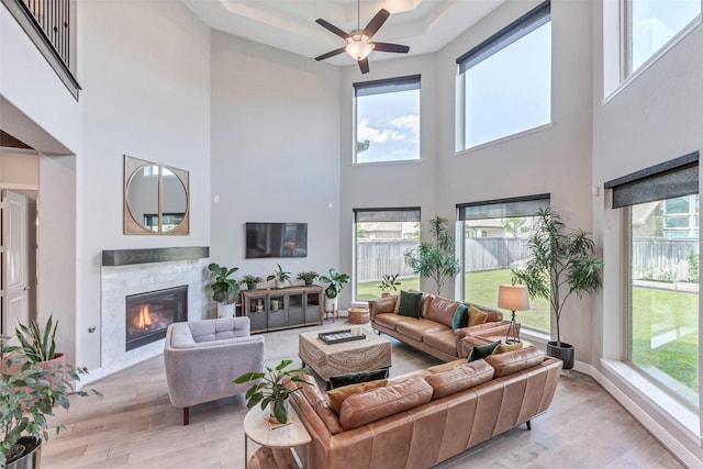 living area featuring a ceiling fan, light wood-style floors, a high ceiling, and a glass covered fireplace