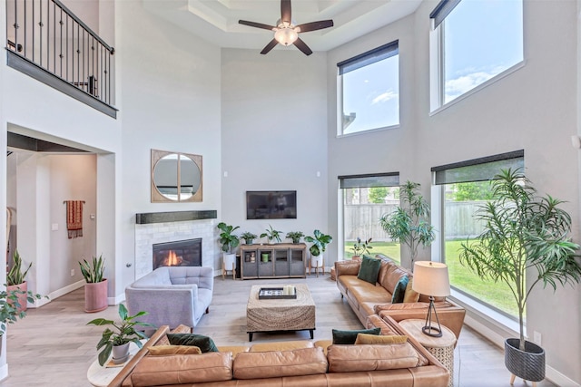 living area featuring a tiled fireplace, ceiling fan, a high ceiling, and wood finished floors