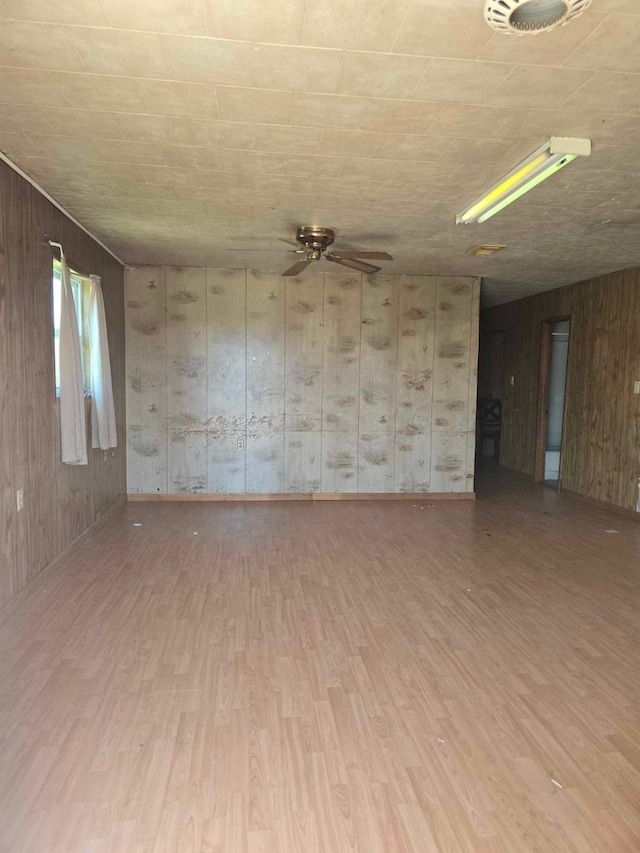 unfurnished room featuring wood walls, a ceiling fan, and wood finished floors