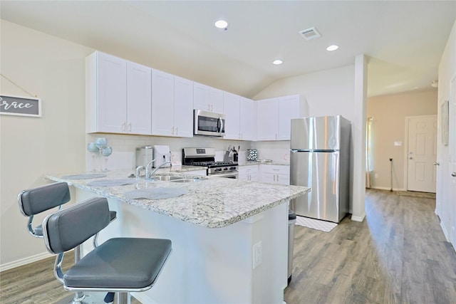 kitchen with a peninsula, white cabinets, a breakfast bar, visible vents, and stainless steel appliances