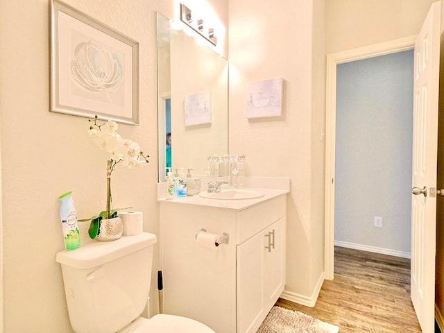 bathroom with toilet, vanity, wood finished floors, and baseboards