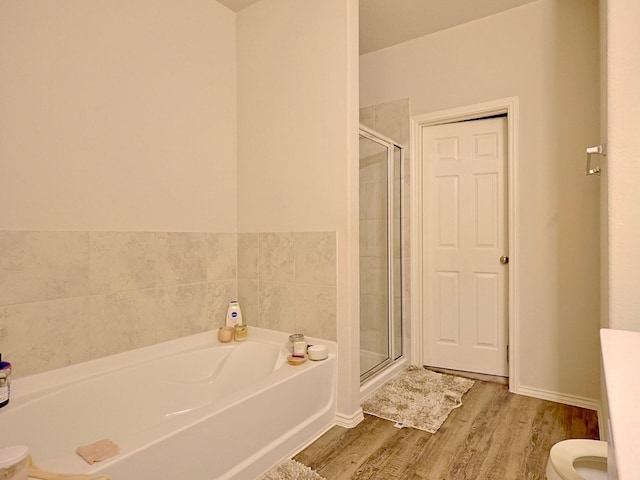 bathroom featuring a shower stall, a garden tub, toilet, and wood finished floors
