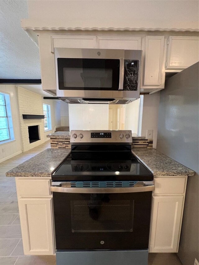 602 Rosewood Dr, Shenandoah, TX 77381 - kitchen featuring appliances with stainless steel finishes, light stone countertops, white cabinetry, open floor plan, and a brick fireplace
