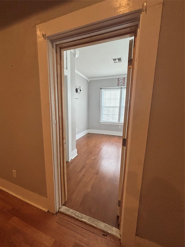 hallway with wood finished floors, crown molding, and baseboards