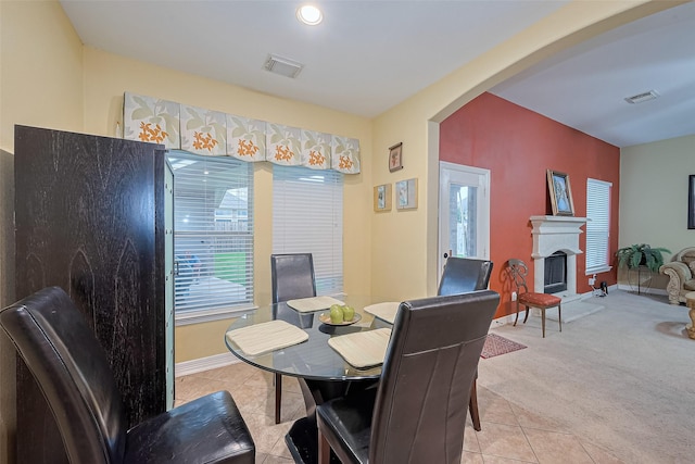 dining space featuring arched walkways, light tile patterned floors, visible vents, and a fireplace with raised hearth