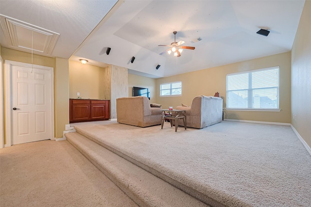 carpeted living area featuring vaulted ceiling, baseboards, attic access, and a ceiling fan