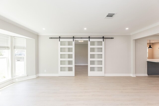 empty room featuring light wood-type flooring, crown molding, visible vents, and a barn door
