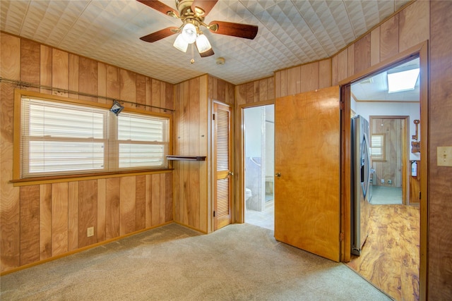 unfurnished bedroom featuring wood walls, stainless steel fridge, ensuite bathroom, and light carpet