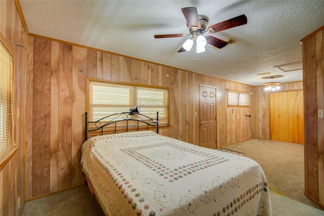 bedroom with a textured ceiling, attic access, wood walls, and carpet