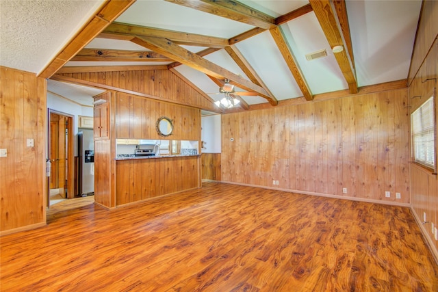 unfurnished living room featuring visible vents, lofted ceiling with beams, ceiling fan, wooden walls, and wood finished floors