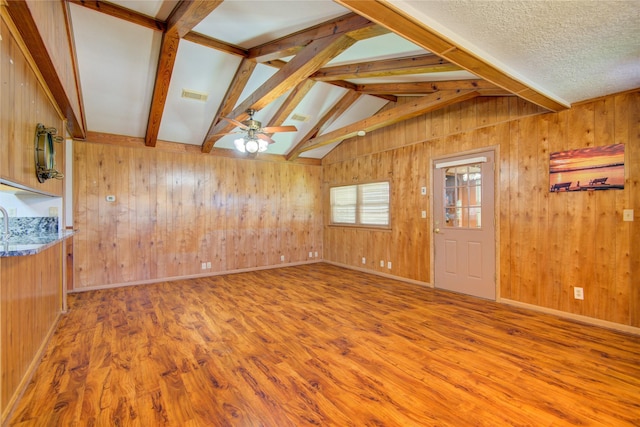 spare room featuring wood walls, lofted ceiling with skylight, visible vents, ceiling fan, and wood finished floors