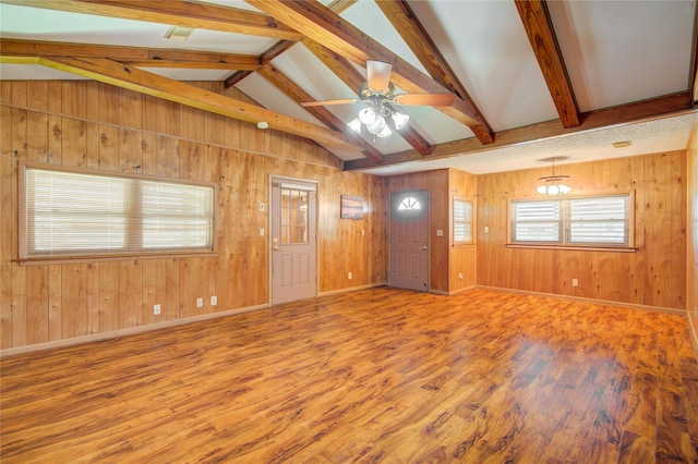 unfurnished living room featuring baseboards, lofted ceiling with beams, wood walls, ceiling fan, and wood finished floors
