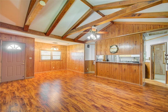 unfurnished living room with wood finished floors, wood walls, lofted ceiling with beams, and a ceiling fan