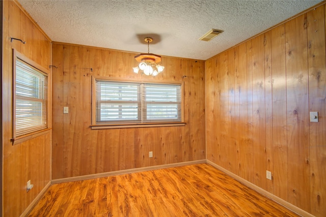 unfurnished room featuring a chandelier, a textured ceiling, wood finished floors, and visible vents