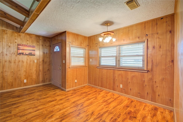 unfurnished dining area with wood walls, visible vents, a textured ceiling, and wood finished floors