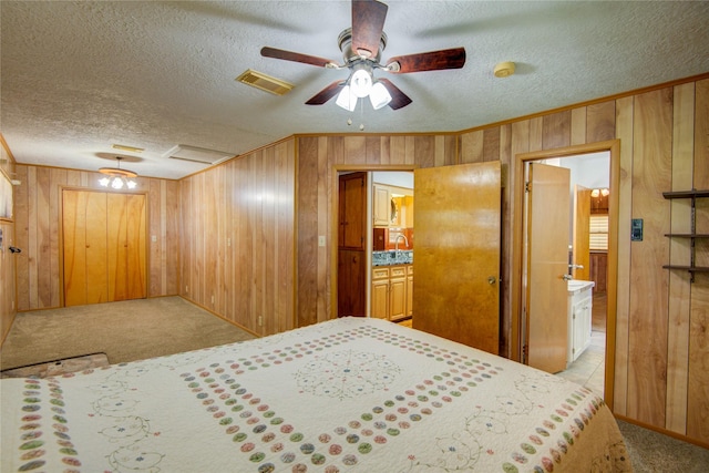 carpeted bedroom with crown molding, ensuite bathroom, a textured ceiling, visible vents, and wooden walls