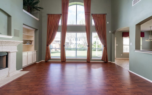 24807 Mason Trail Dr, Katy, TX 77493 - unfurnished living room featuring a fireplace, arched walkways, a towering ceiling, visible vents, and baseboards