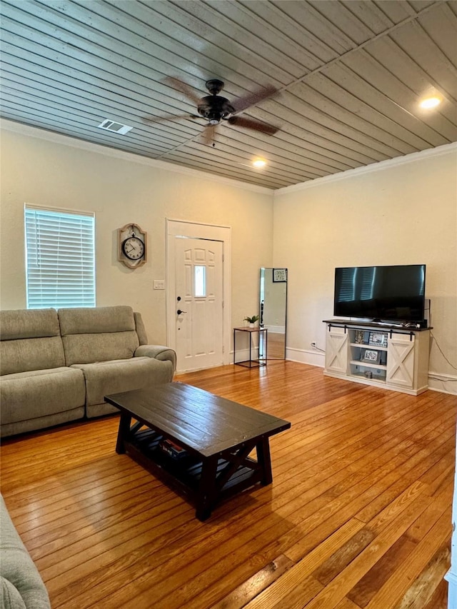 living area featuring crown molding, ceiling fan, visible vents, wood-type flooring, and baseboards