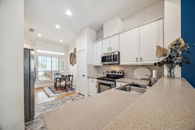 kitchen featuring visible vents, white cabinets, a sink, stainless steel appliances, and backsplash