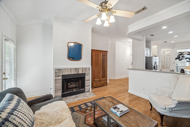 living area with visible vents, baseboards, ceiling fan, a fireplace, and light wood finished floors