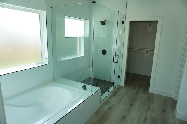 bathroom with a shower stall, a walk in closet, a garden tub, and wood finished floors