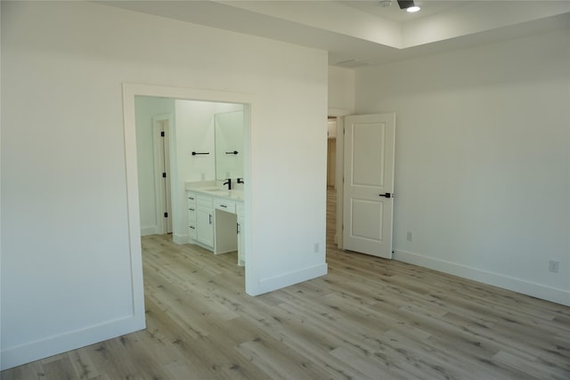 unfurnished bedroom with a sink, ensuite bathroom, light wood-style flooring, and baseboards