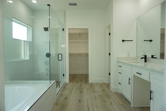 bathroom with a spacious closet, a shower stall, visible vents, a bath, and wood finished floors