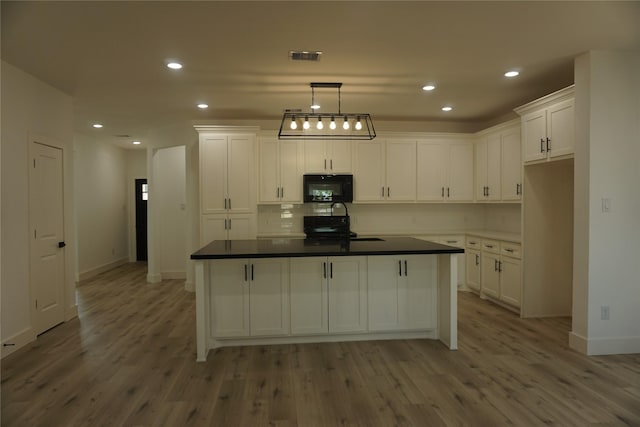 kitchen with a sink, black microwave, and white cabinetry