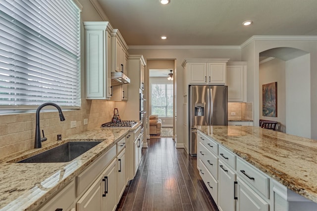 271 Spotted Saddle Ct, The Woodlands, TX 77382 - kitchen with arched walkways, appliances with stainless steel finishes, light stone counters, a sink, and under cabinet range hood