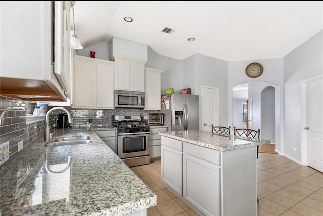 kitchen featuring visible vents, arched walkways, a sink, appliances with stainless steel finishes, and decorative backsplash