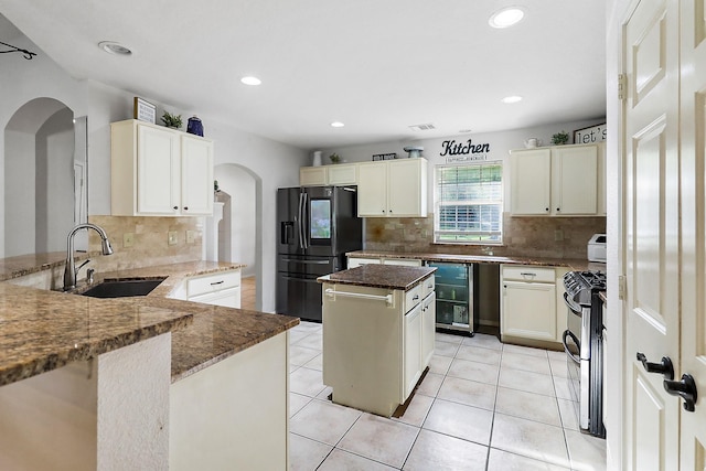 kitchen featuring stainless steel gas stove, dark stone counters, a sink, black fridge with ice dispenser, and decorative backsplash