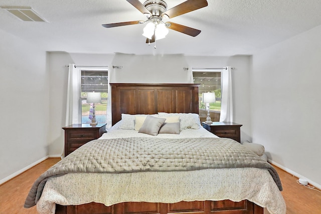 bedroom with light wood finished floors, ceiling fan, baseboards, and visible vents