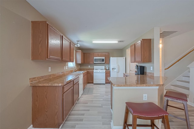 kitchen with a peninsula, white appliances, a kitchen bar, a sink, and light wood-style flooring