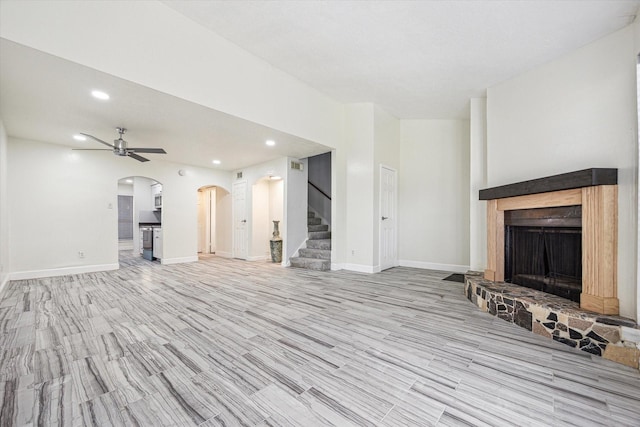 unfurnished living room with recessed lighting, stairway, a fireplace with raised hearth, a ceiling fan, and arched walkways