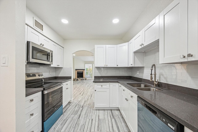 kitchen with stainless steel appliances, a sink, arched walkways, decorative backsplash, and white cabinetry